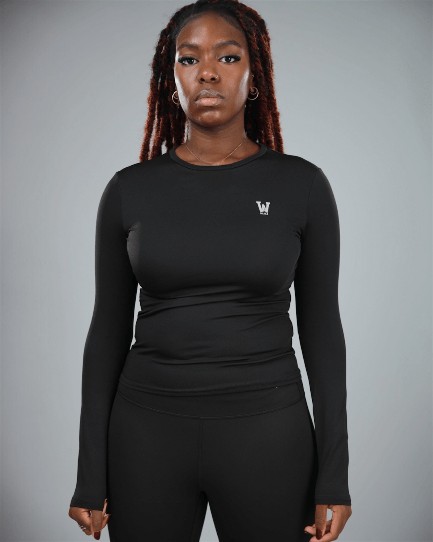 Person wearing a black long-sleeve athletic top with waaka logo on a gray background