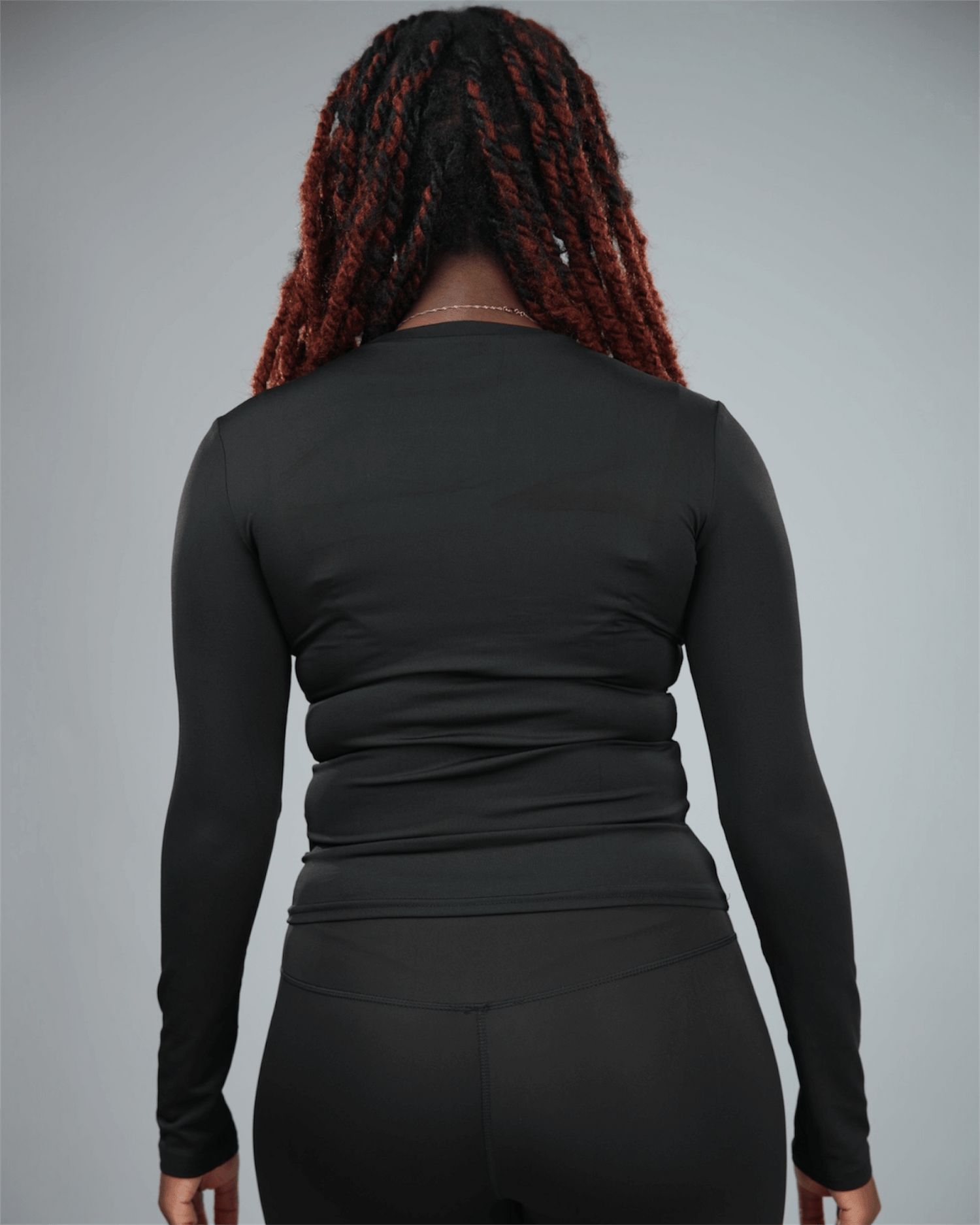 Person wearing a black long-sleeve top against a gray background back view