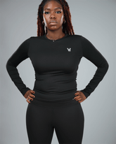 Person wearing a black long-sleeve top with waaka logo on a gray background with arms by her side