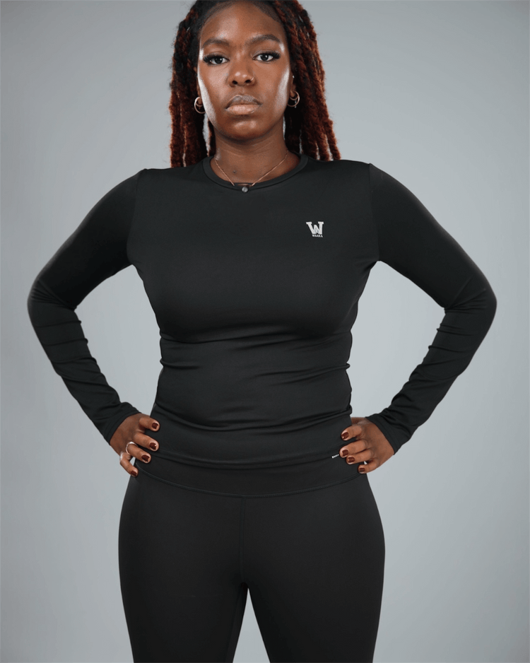 Person wearing a black long-sleeve top with waaka logo on a gray background with arms by her side