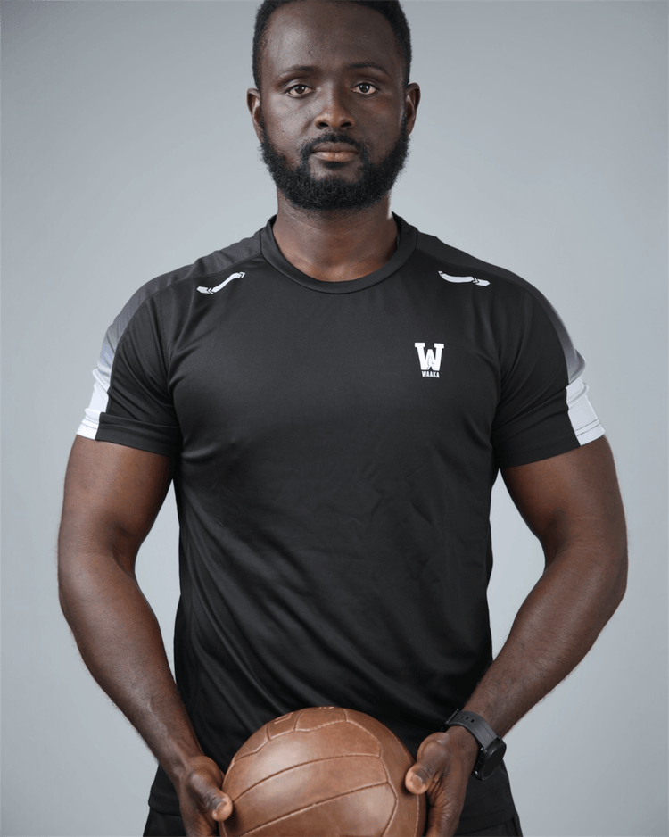 Man holding a medicine ball wearing a black sports shirt with waaka logo on a gray background