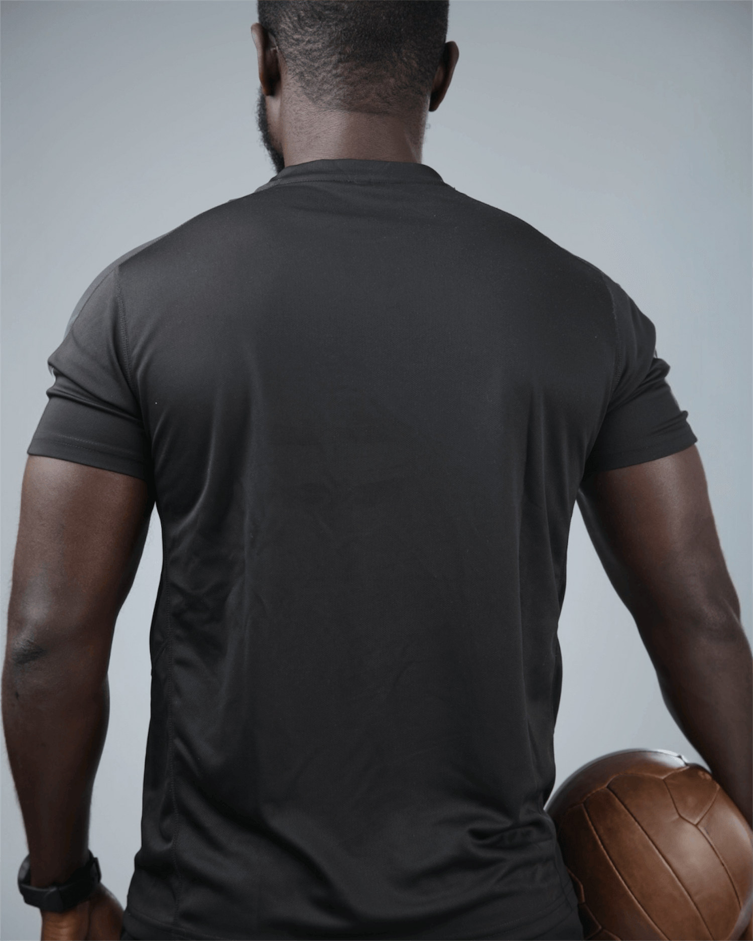 Man wearing the black grey eco training t-shirt holding a medicine ball against a gray background back view