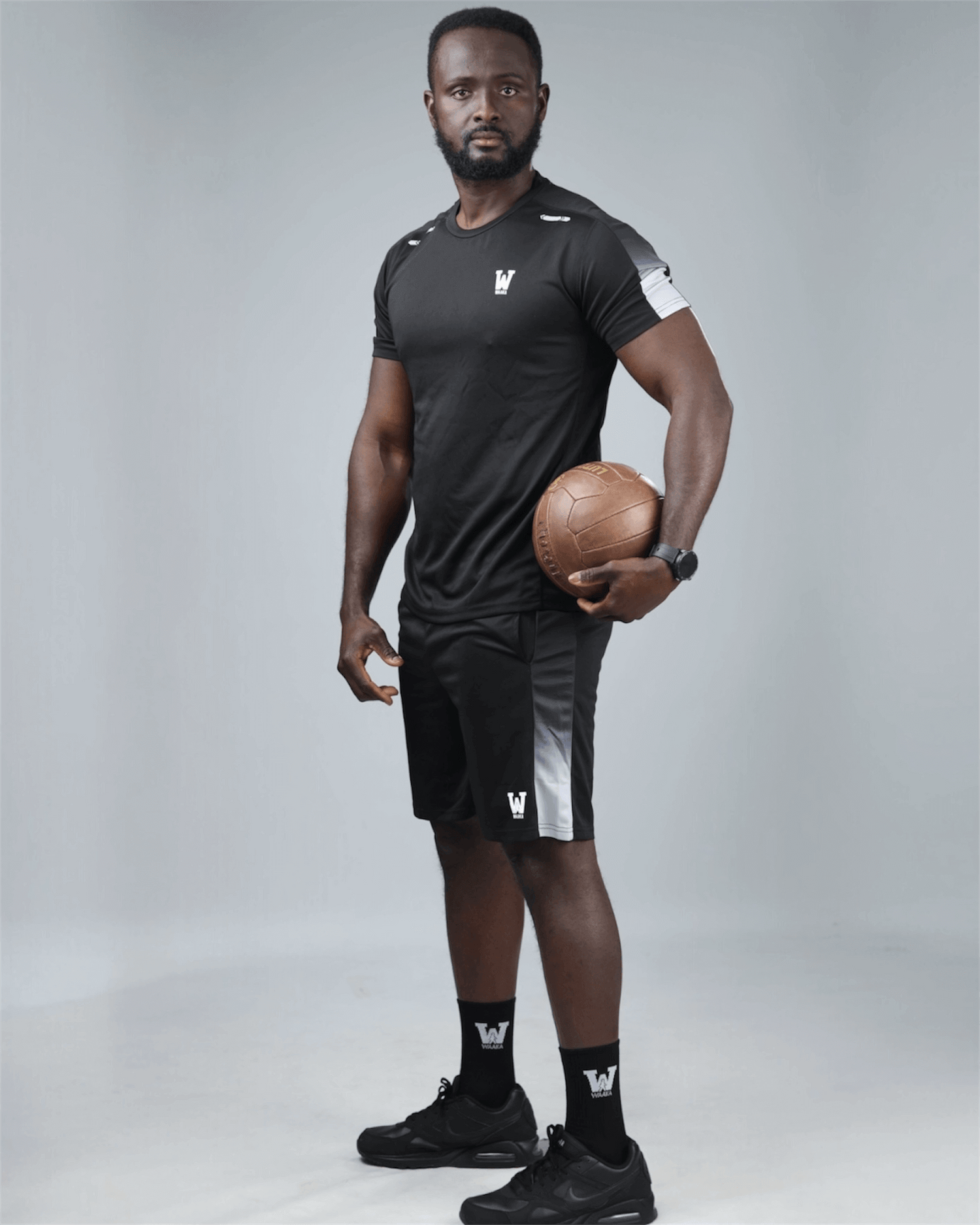 Man in black grey athletic wear holding a basketball against a gray background