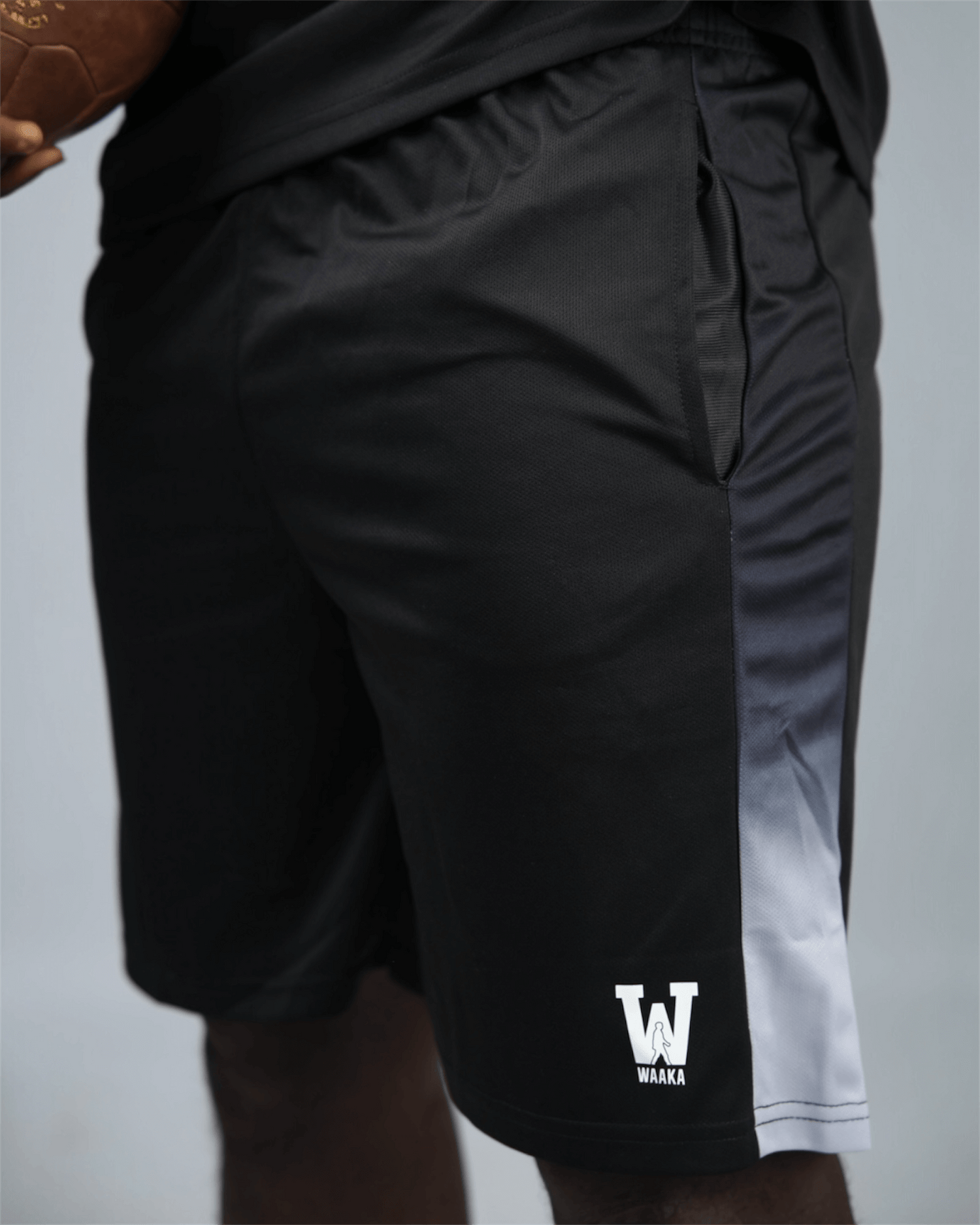 Black eco training athletic shorts with a white waaka logo on a grey background