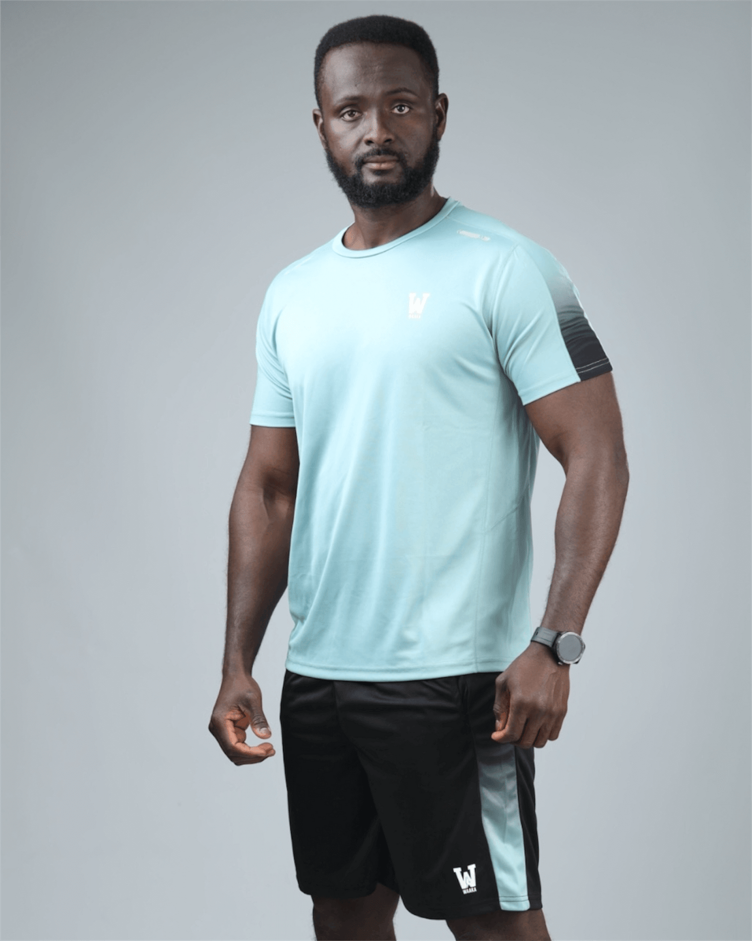 Man wearing a light blue athletic shirt and black shorts on a gray background