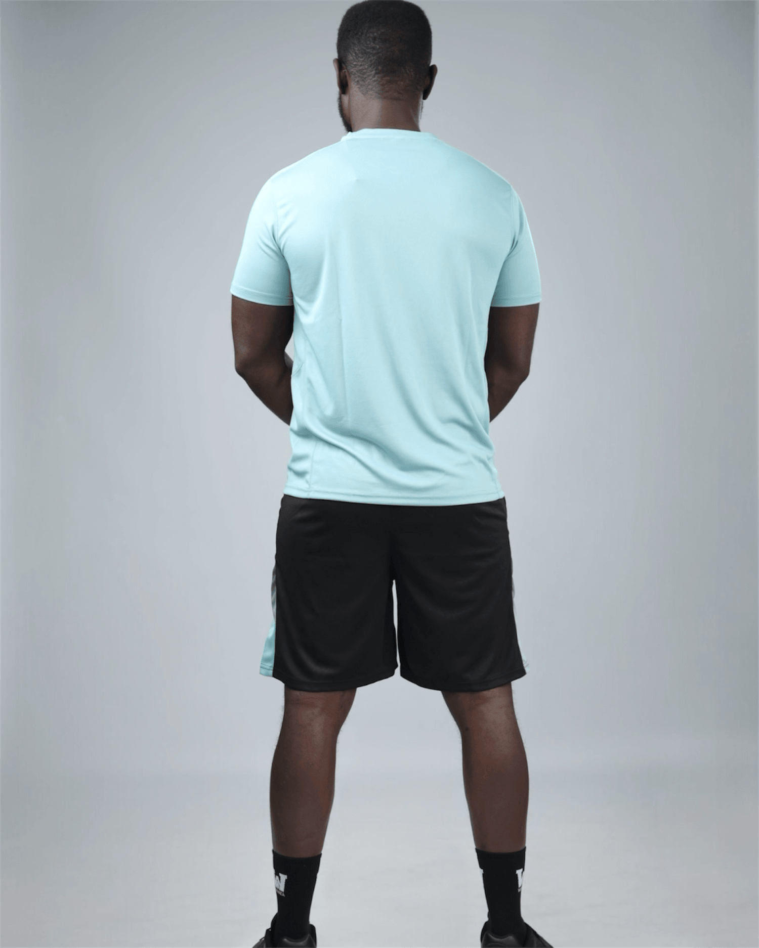 Person wearing a light blue t-shirt and black shorts on a gray  background back view