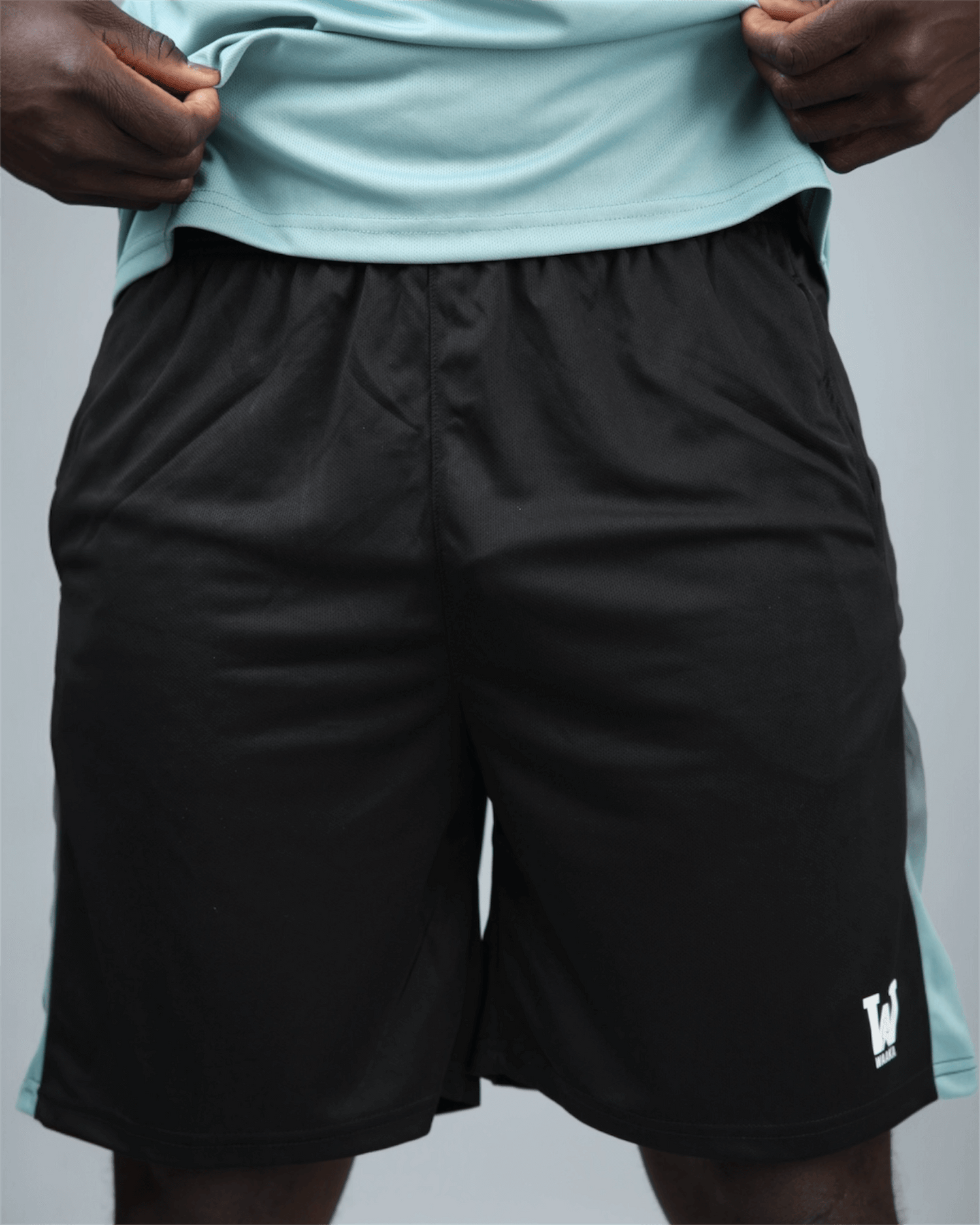 Black eco training shorts with a light blue stripe featuring waaka logo on a grey background front view