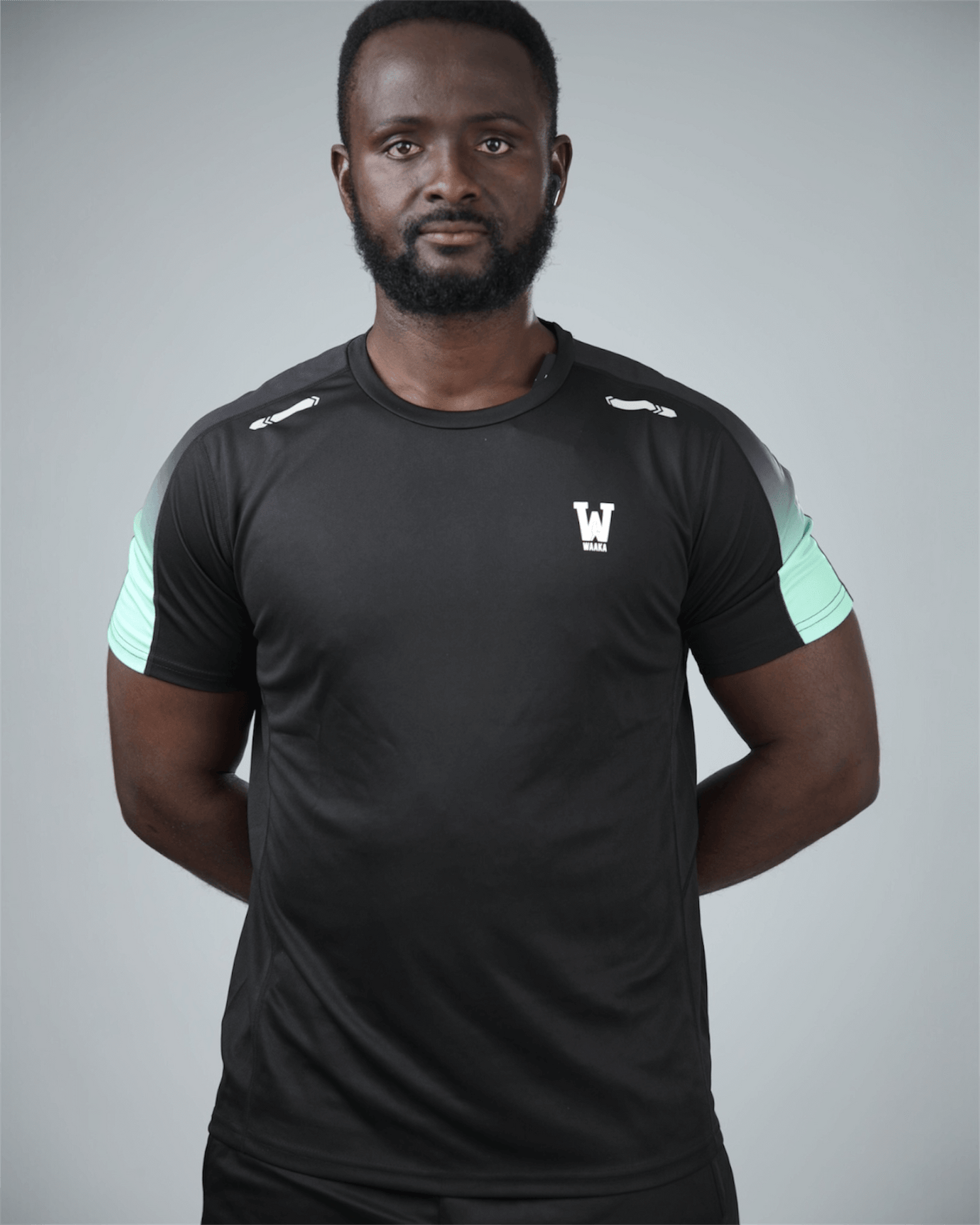 Man wearing a black athletic outfit with waaka logo on a grey studio background