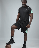 Man wearing a black athletic outfit with a logo, posing with a sports ball on a gray background