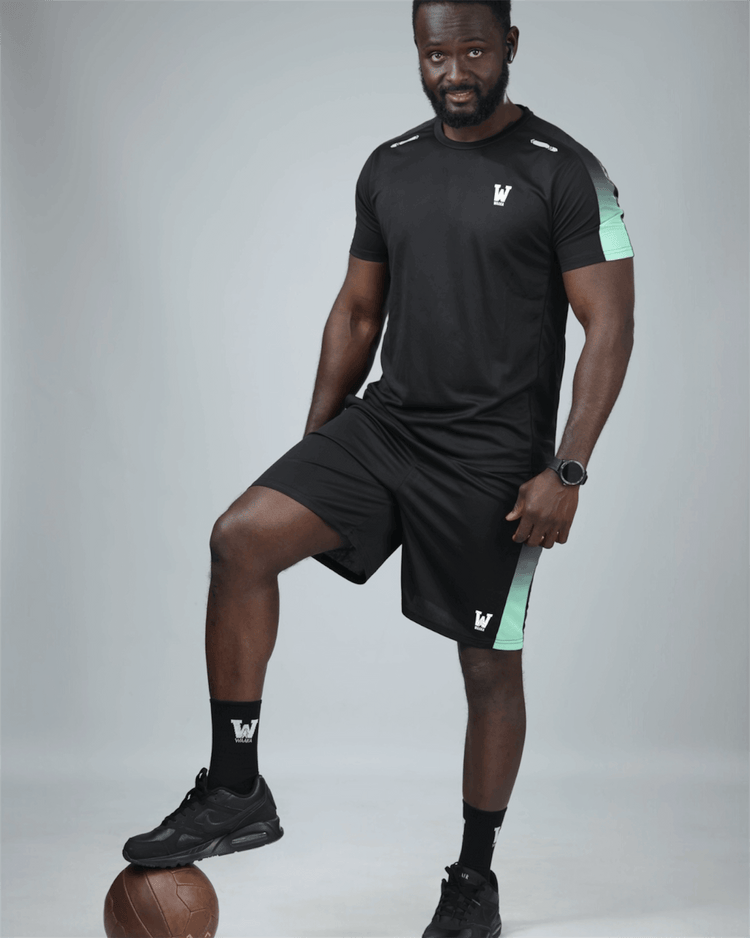 Man wearing a black athletic outfit with a logo, posing with a sports ball on a gray background