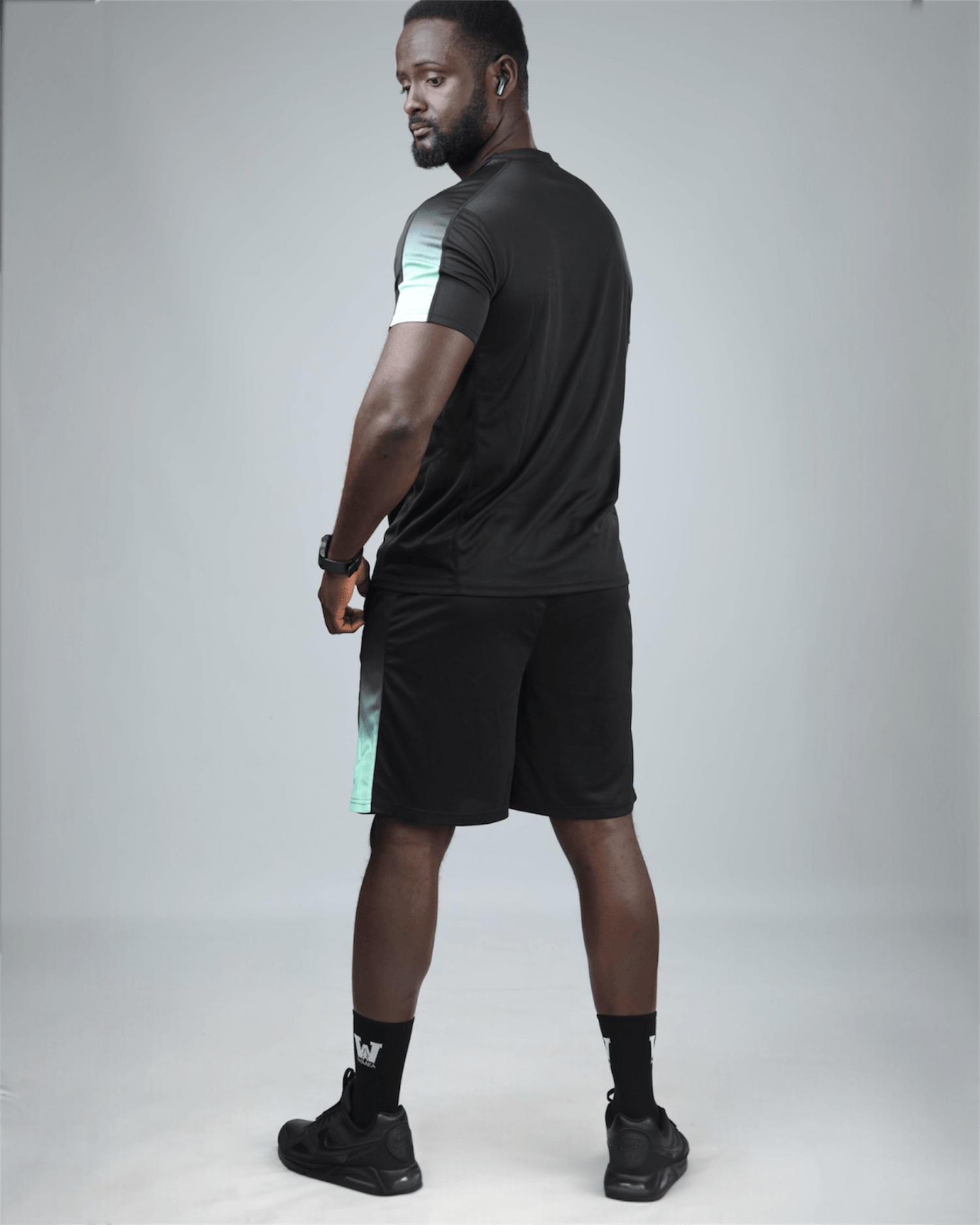 Man wearing a black athletic outfit with a gray background back view