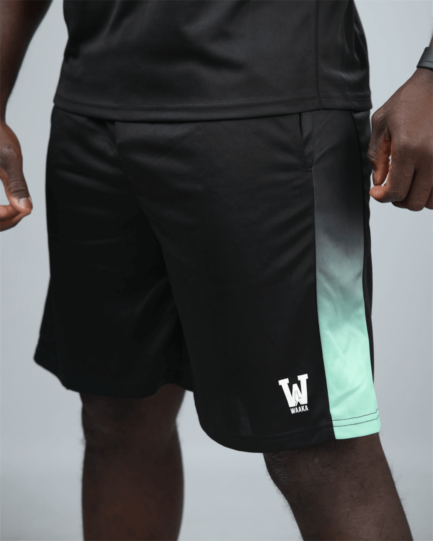 Black eco training shorts with waaka logo an green accents on a grey background