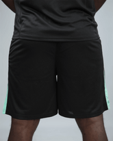 Black eco training shorts with waaka logo an green accents on a grey background back view