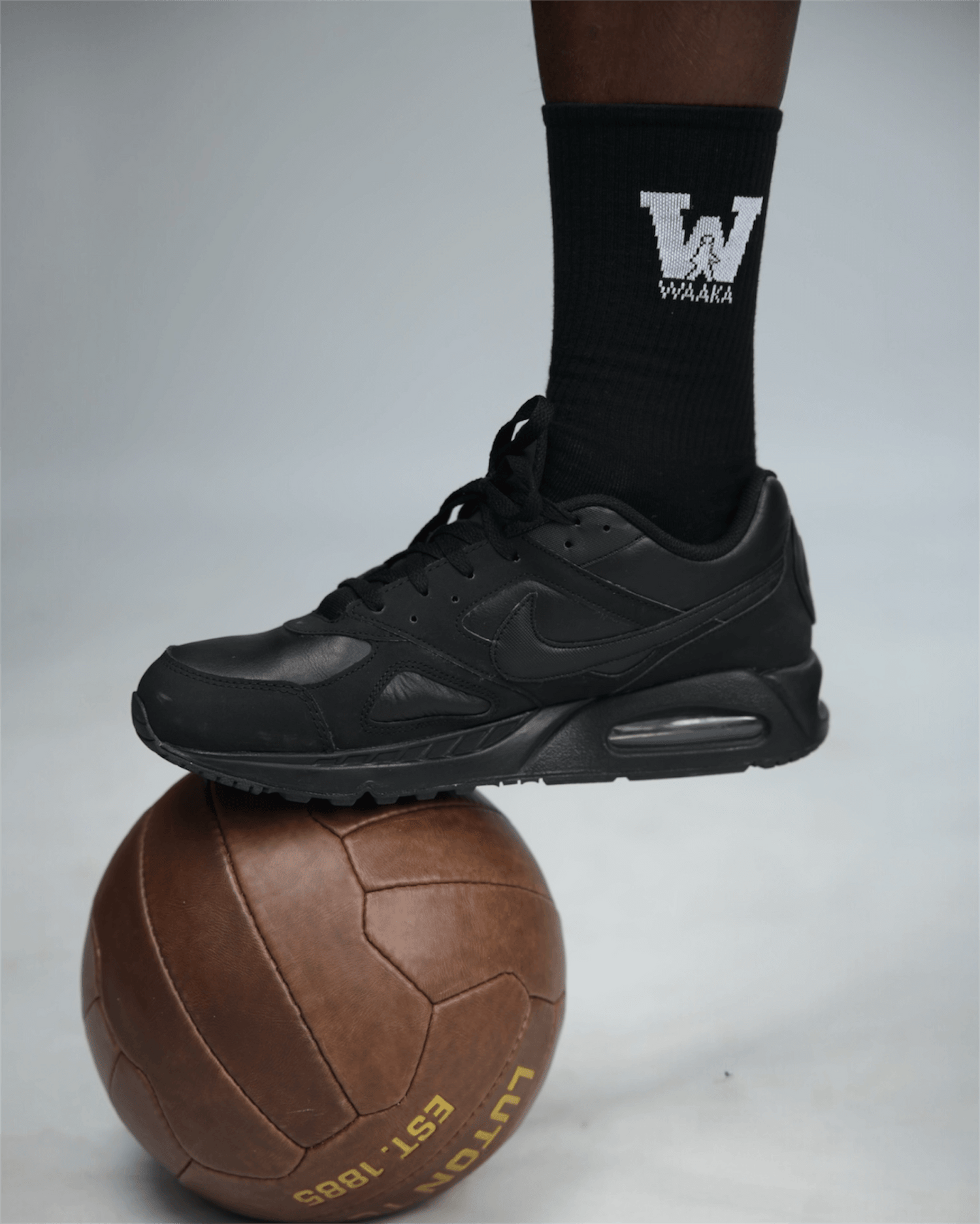 Black athletic shoe and sock with waaka logo on a gray background