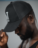 Man wearing a black cap with waaka logo, looking downwards.