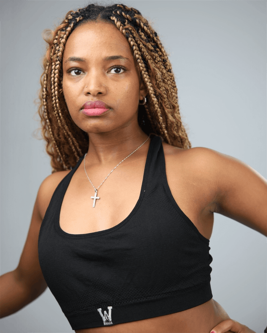 Woman wearing a black sports bra with waaka  logo on a grey background