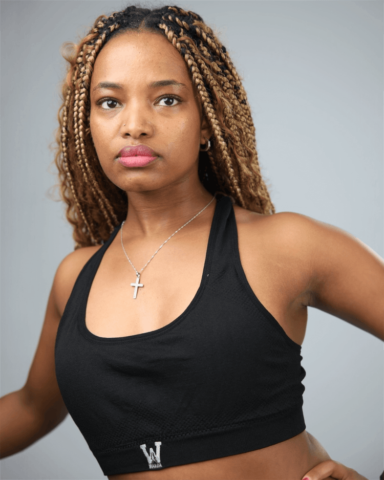Woman wearing a black sports bra with waaka  logo on a grey background