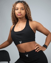 Woman wearing a black sports bra and leggings with waaka logo, standing against a gray background.
