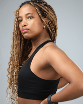 Woman with long braided hair wearing waaka black sports bra against a gray background