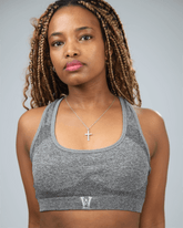 Woman wearing a grey sports bra with waaka logo on a plain background