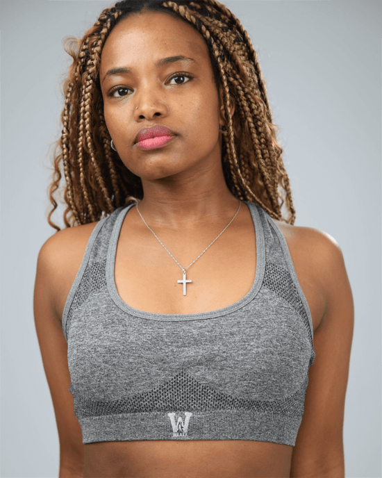 Woman wearing a grey sports bra with waaka logo on a plain background