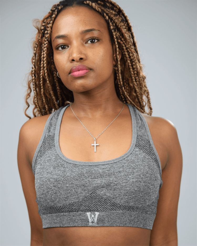 Woman wearing a grey sports bra with waaka logo on a plain background
