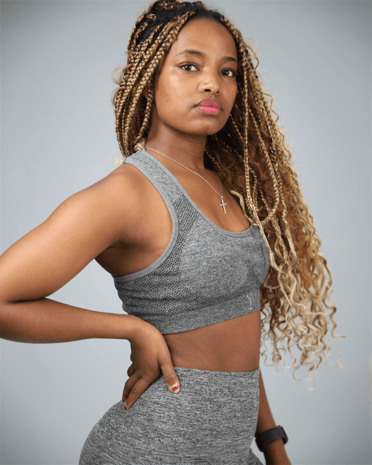 Woman wearing a gray athletic outfit against a plain background side view