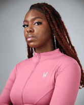 Woman wearing a pink long-sleeve top with a logo on a gray background