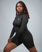 Person wearing a black athletic outfit with a logo on a gray background stretching