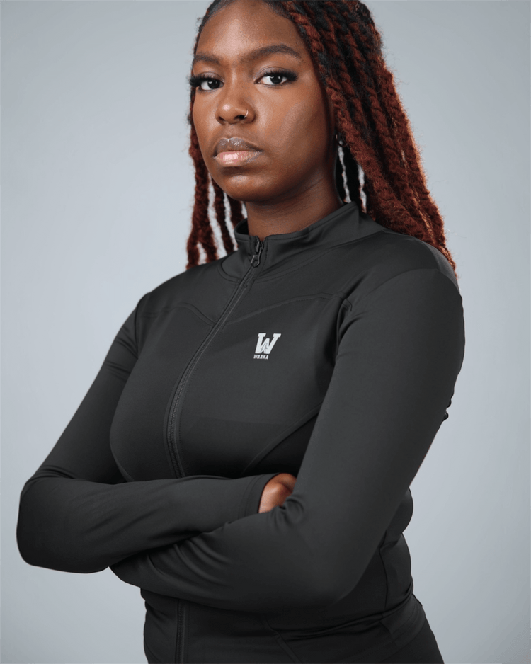 Person wearing a black athletic jacket with waaka logo on a gray background