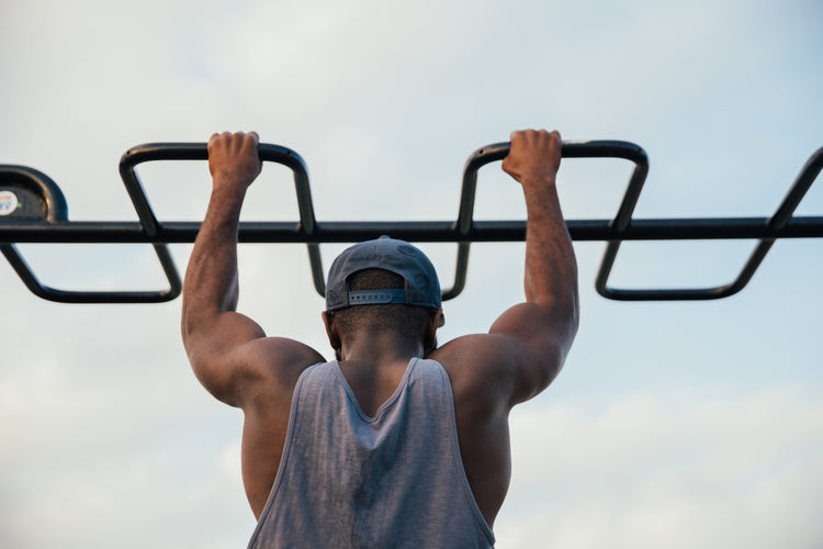 Man in athletic tank top and cap doing pull-ups on outdoor fitness bar